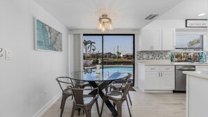 A modern kitchen with a dining area, large windows, and a view of a swimming pool.