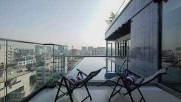 A modern balcony with glass railings, two lounge chairs, and a view of a cityscape.