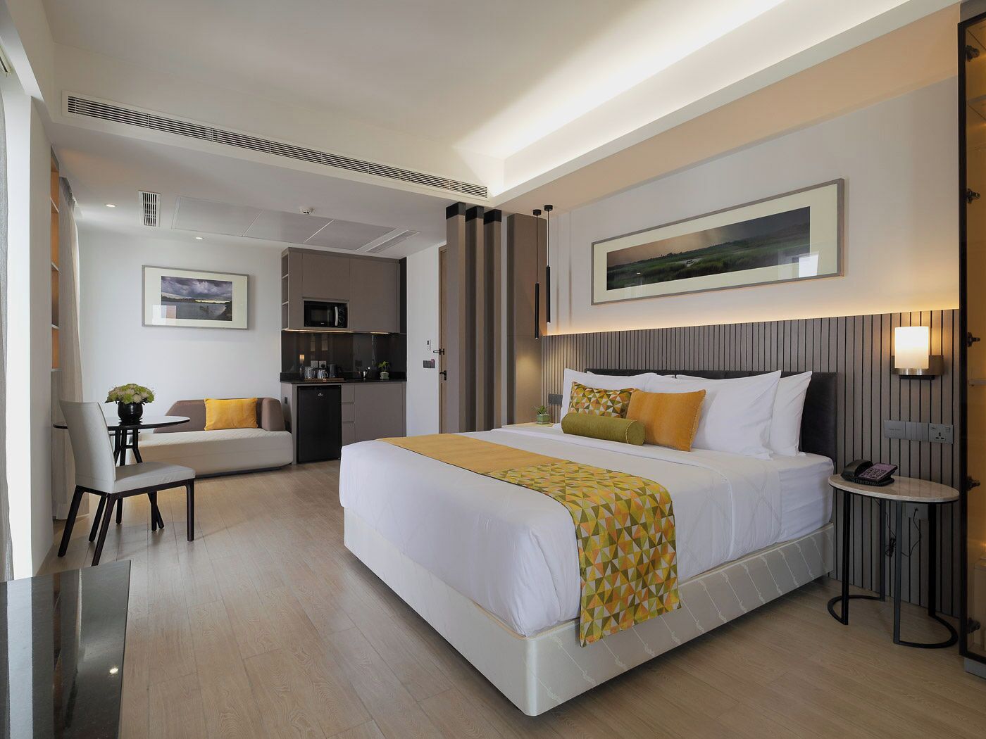 A hotel room with a large bed, a desk, a chair, a small kitchenette, and a dining area.