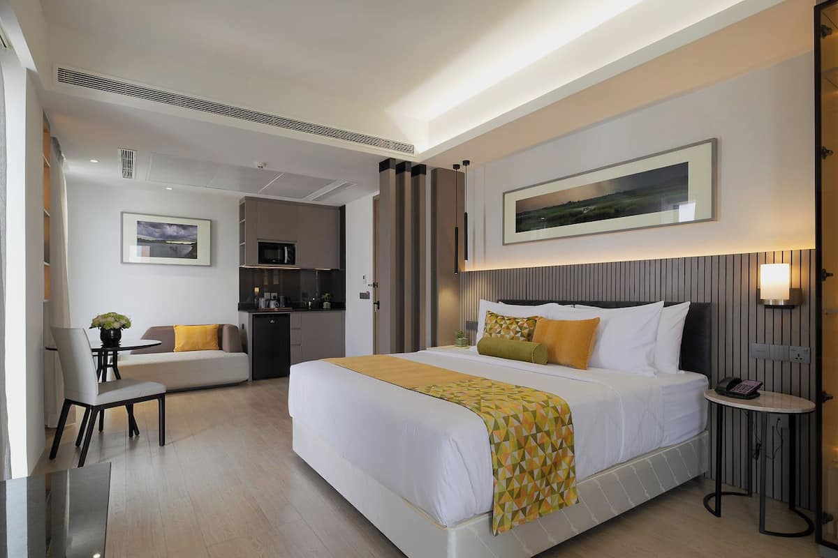 Una habitación de hotel con una cama grande, un escritorio, una silla, una kitchenette pequeña y una zona de comedor.