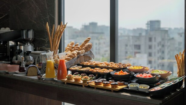 Un bufé de desayuno con diversos pasteles, frutas y bebidas, con vistas a la ciudad.