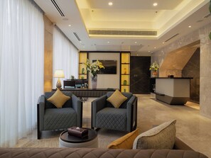A modern hotel lobby with two armchairs, a round coffee table, a reception desk, and a large mirror. - W Residence Living (Dhaka)