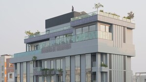 Un moderno edificio de gran altura con múltiples balcones, ventanas amplias y un jardín en la azotea.