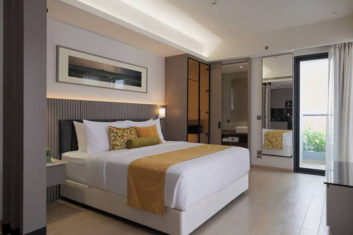 Habitación de hotel moderna con una cama grande, una mesita de noche, un espejo y vistas al exterior.