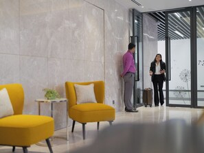 A modern lobby with marble walls, a glass door entrance, and yellow armchairs. - W Residence Living (Dhaka)