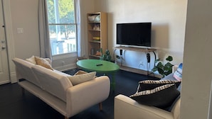 Uma sala de estar com um sofá, uma mesinha, uma televisão sobre um móvel e uma estante de livros.