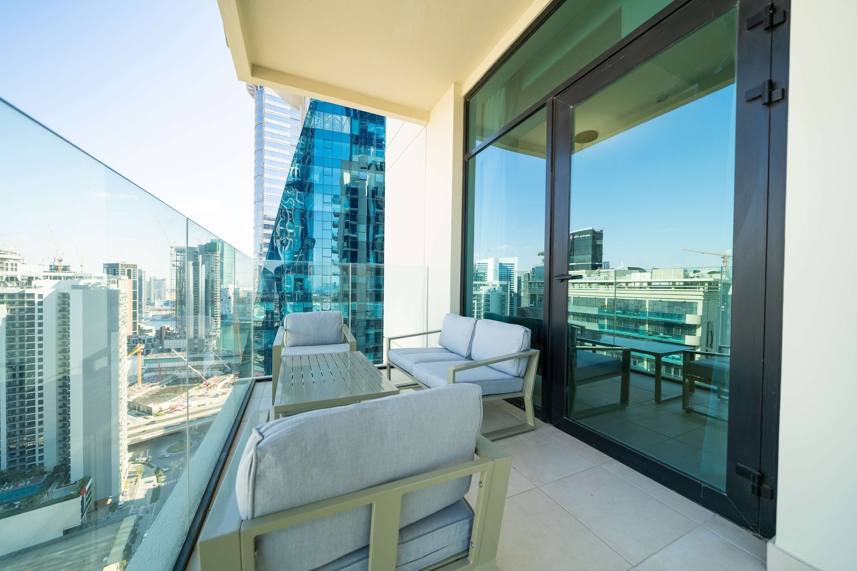 Un balcon avec deux canapés de couleur gris clair, une petite table et une porte vitrée donnant sur une vue de la ville.