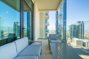 A balcony with a sofa, a chair, and a table, overlooking a cityscape with high-rise buildings.