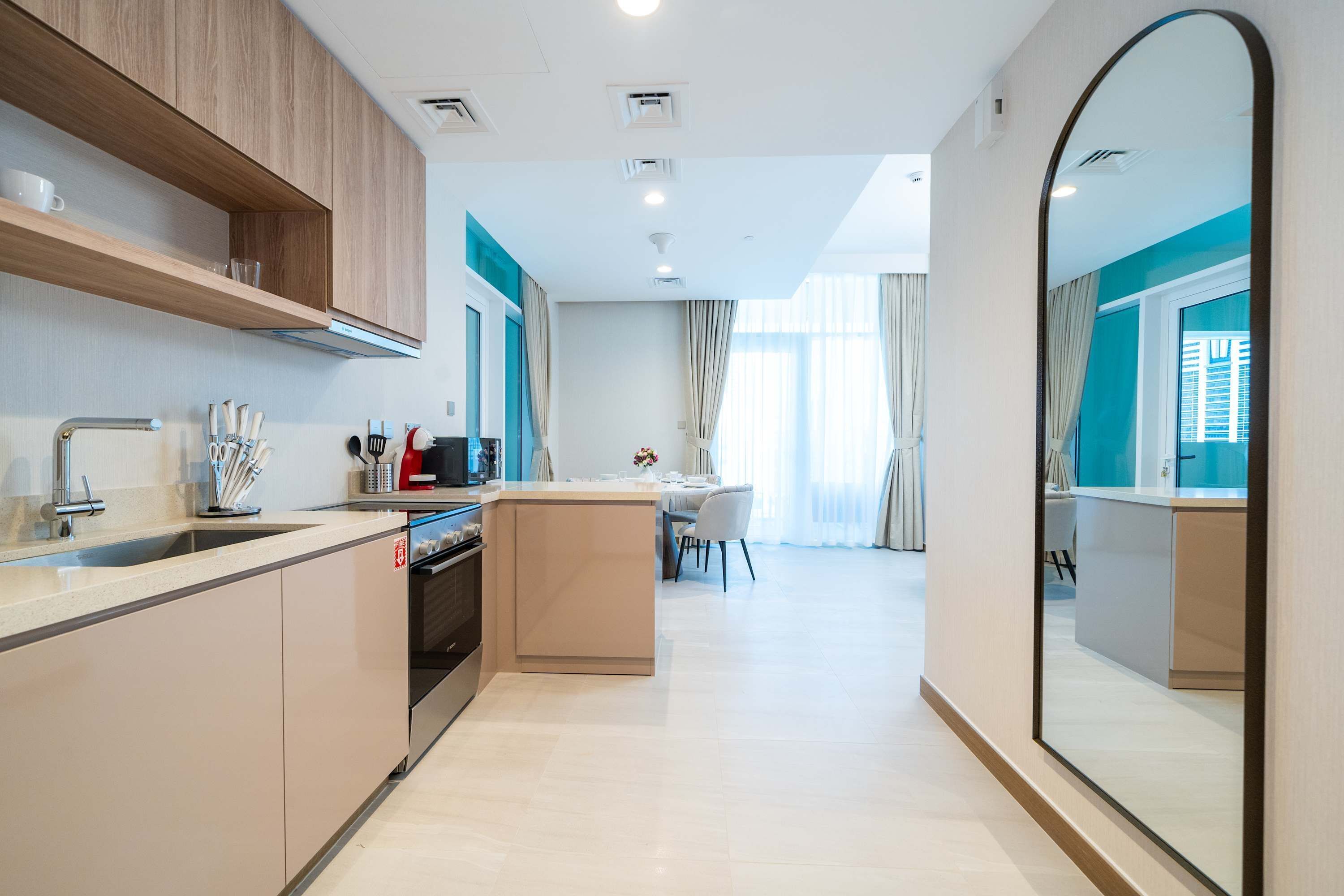 Une cuisine moderne dotée d’un îlot central, d’un coin repas avec une table et des chaises, et d’un grand miroir qui reflète la pièce.