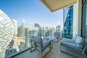 Un balcon doté d’une balustrade en verre, deux canapés gris, une petite table et une vue sur les bâtiments de la ville.
