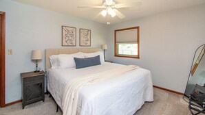 Quarto com cama, mesas de cabeceira, ventilador de teto e quadros na parede.