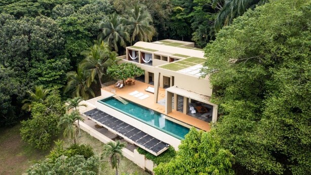 A modern villa with a swimming pool, surrounded by lush greenery and palm trees.
