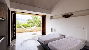 A modern bedroom with two beds, a hammock, and a view of greenery.