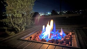 A fire pit with burning logs at night, surrounded by a metal fence and a tree. - Atomic Arcade: Mid-Century Getaway with Games & Pool (Yucca Valley)