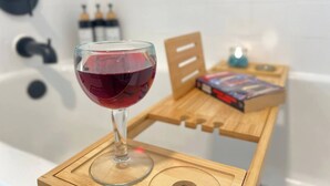A glass of red wine on a wooden tray in a bathroom with a bathtub, a wooden chair, and a box of tissues. - Atomic Arcade: Mid-Century Getaway with Games & Pool (Yucca Valley)