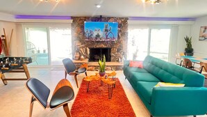 A spacious living room with a stone fireplace, a television, and a pool table. - Atomic Arcade: Mid-Century Getaway with Games & Pool (Yucca Valley)