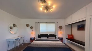 A modern bedroom with a large bed, a desk, and a bench. - Atomic Arcade: Mid-Century Getaway with Games & Pool (Yucca Valley)