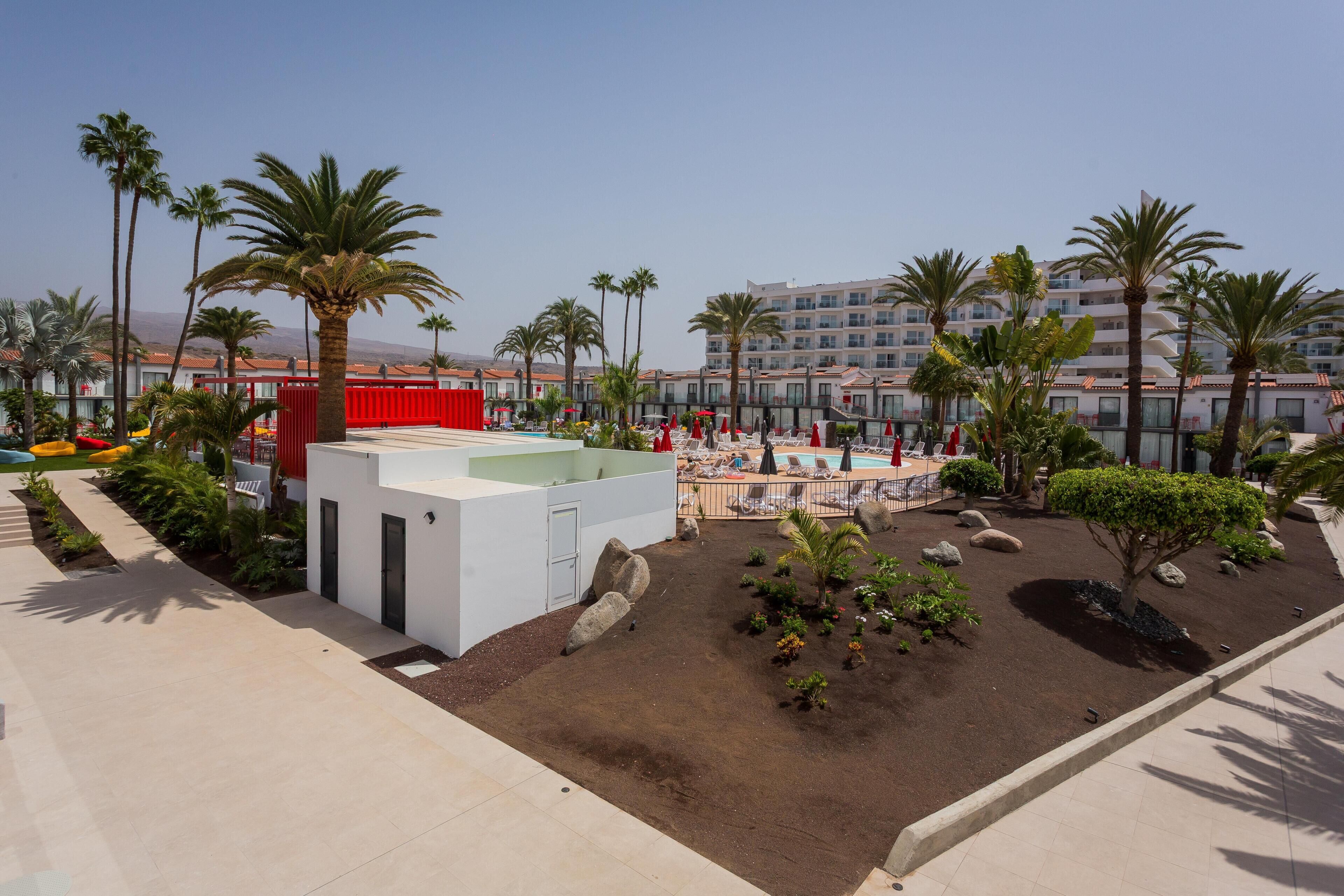 A resort with a pool area, palm trees, and a building with a red facade.
