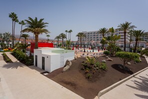 A resort with a pool area, palm trees, and a building with a red facade. - Sholeo Lodges Maspalomas (San Bartolomé de Tirajana)