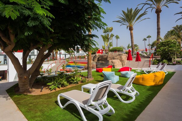 An outdoor seating area with lounge chairs, a tree, and a rock formation. - Sholeo Lodges Maspalomas (San Bartolomé de Tirajana)