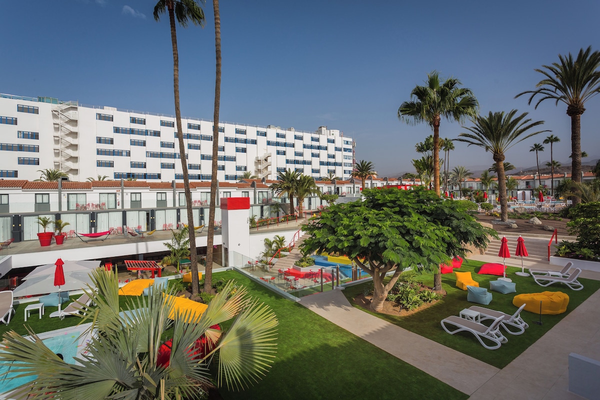 A hotel with a pool area, outdoor seating, and palm trees.