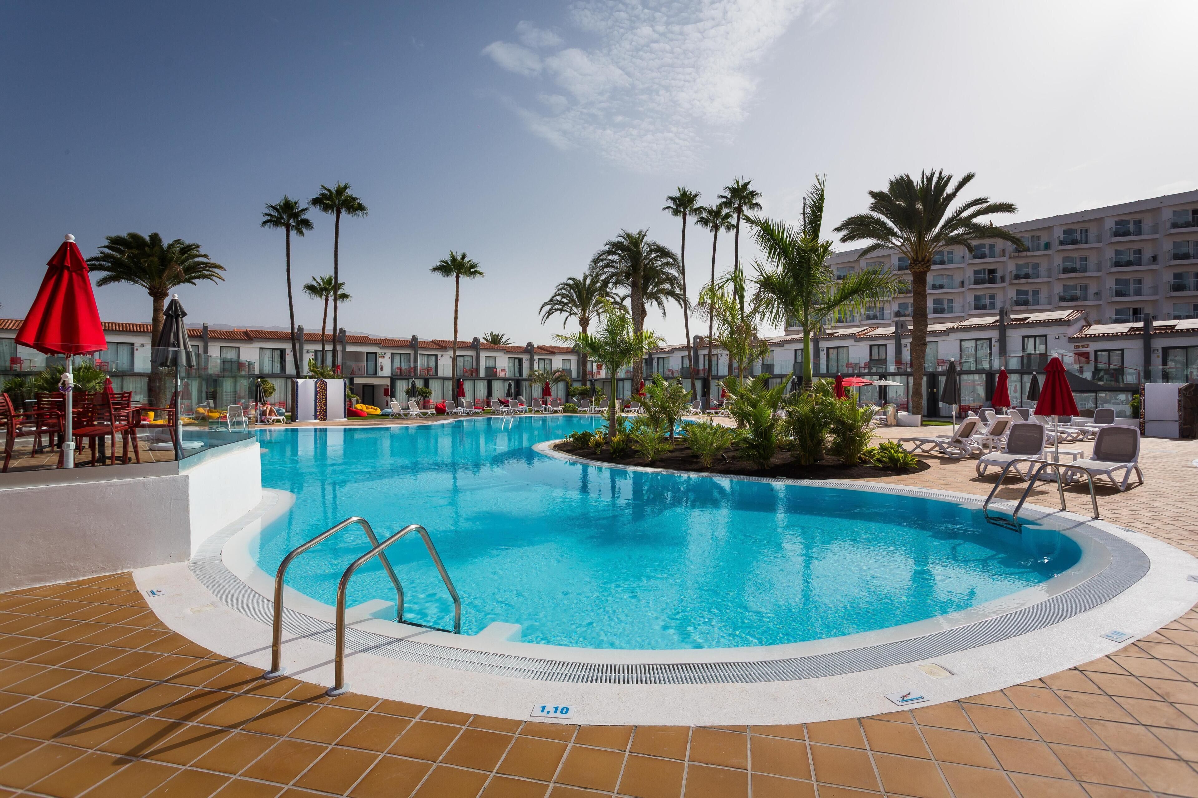 Ein Schwimmbecken mit Fliesenveranda, Liegestühlen und Palmen.