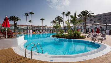 Ein Schwimmbecken mit Fliesenveranda, Liegestühlen und Palmen.
