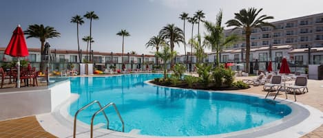 A swimming pool with a tiled deck, lounge chairs, and palm trees.