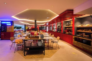 A modern restaurant with multiple tables and chairs, a counter with food displays, and a sign indicating amenities like a restaurant, pool, and laundry. - Sholeo Lodges Maspalomas (San Bartolomé de Tirajana)