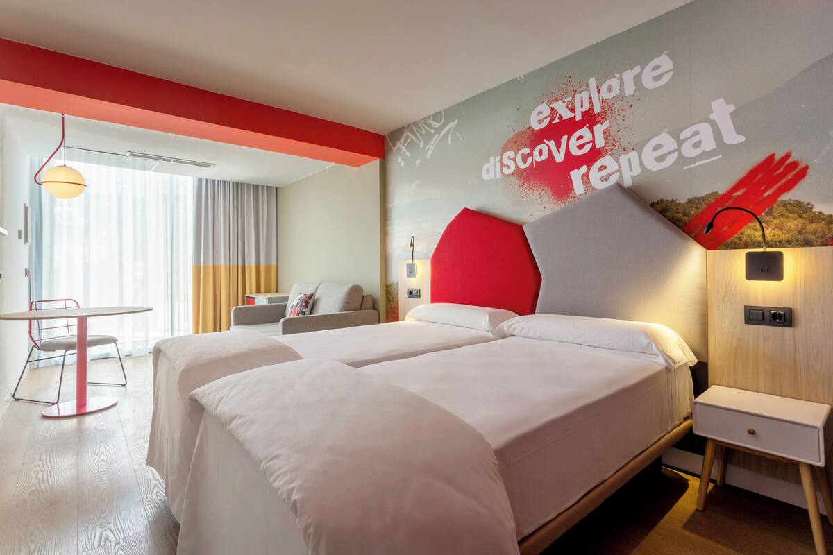 A modern hotel room with two beds, a desk, and a wall with motivational text.