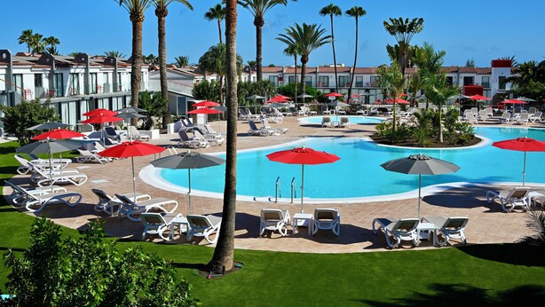 Ein Resort mit mehreren Swimmingpools, Liegestühlen und Palmen.