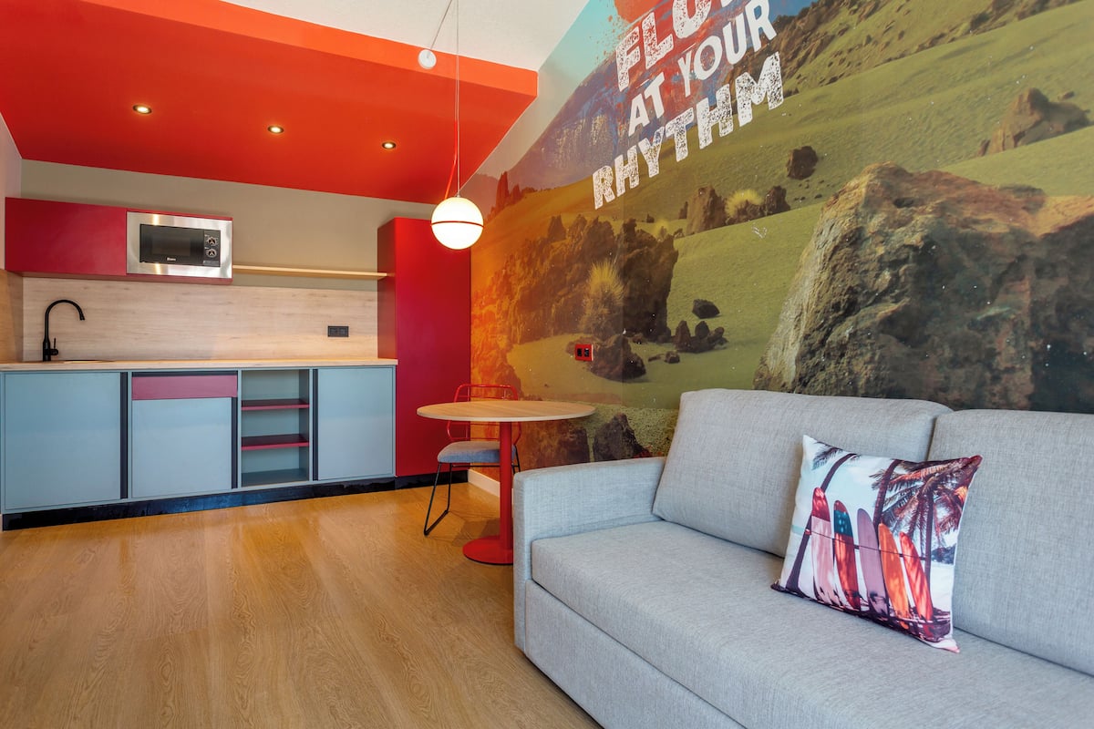 A modern kitchen with a microwave, a dining table with chairs, and a sofa with a decorative pillow.
