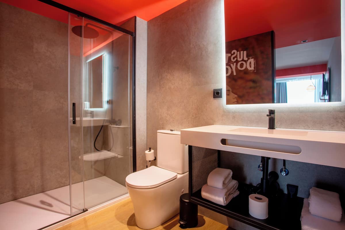 A modern bathroom with a glass shower enclosure, a toilet, and a sink with a towel rack.
