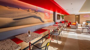 Ein modernes Restaurant mit einer Wüstenmalerei, Holztischen und roten Akzenten.