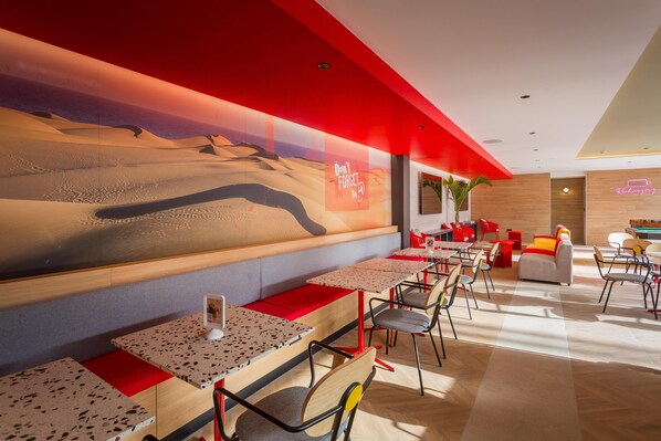 A modern restaurant with a desert-themed mural, wooden tables, and red accents. - Sholeo Lodges Maspalomas (San Bartolomé de Tirajana)