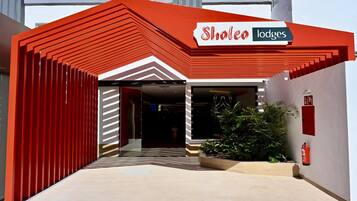 Entrada de un hotel con fachada roja y blanca, un cartel que dice 'Sholeo lodges' y un extintor de incendios en la pared.