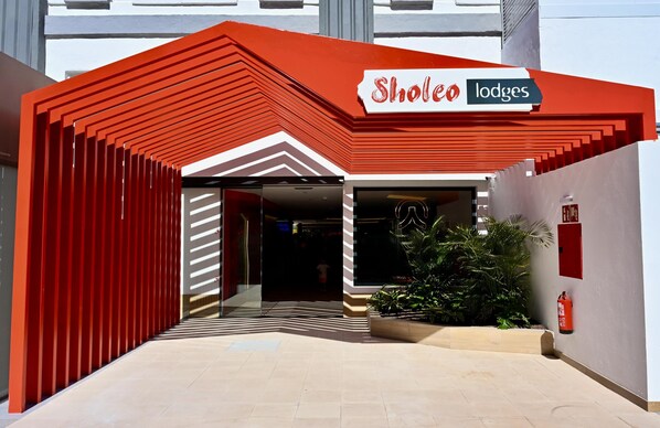 A hotel entrance with a red and white facade, a sign reading 'Sholeo lodges,' and a fire extinguisher mounted on the wall. - Sholeo Lodges Maspalomas (San Bartolomé de Tirajana)