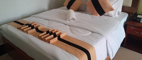 Un lit bien fait, recouvert d’une couverture blanche et beige, avec deux oreillers et une serviette enroulée.