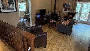 A spacious living room with a fireplace, a ceiling fan, and a staircase leading to another level.