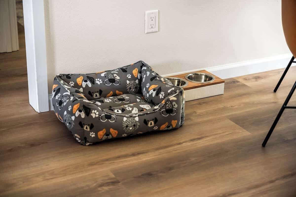A pet bed with a paw print pattern, a feeding station, and a wooden floor.