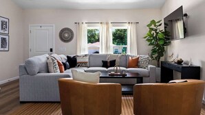 A modern living room with a grey sofa, two wooden chairs, a coffee table, and a large window with curtains.