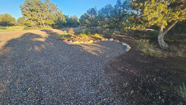 Un camino de grava con un borde circular de piedra, rodeado de árboles y follaje.