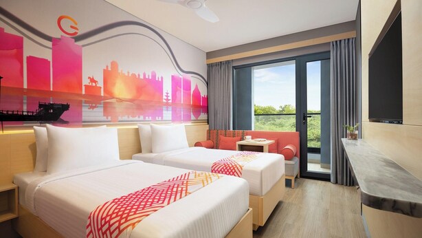 A hotel room with two beds, a balcony with a view, a ceiling fan, and a large window. - Ginger Udaipur, Shastri Circle (Udaipur)