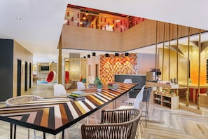A modern interior with a long dining table, comfortable seating, a TV, and a staircase with a unique design. - Ginger Udaipur, Shastri Circle (Udaipur)
