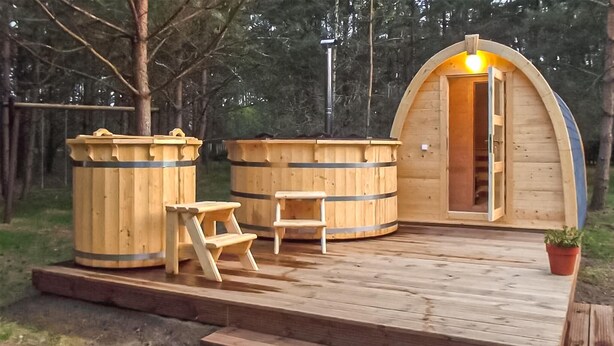 A wooden cabin with a porch, two wooden barrels, a small wooden table, and a potted plant. - Beautiful home in Karsin with sauna (Karsin)