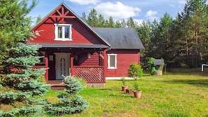 A red wooden house with a sloped roof, a front porch, and a small garden with potted plants. - Beautiful home in Karsin with sauna (Karsin)