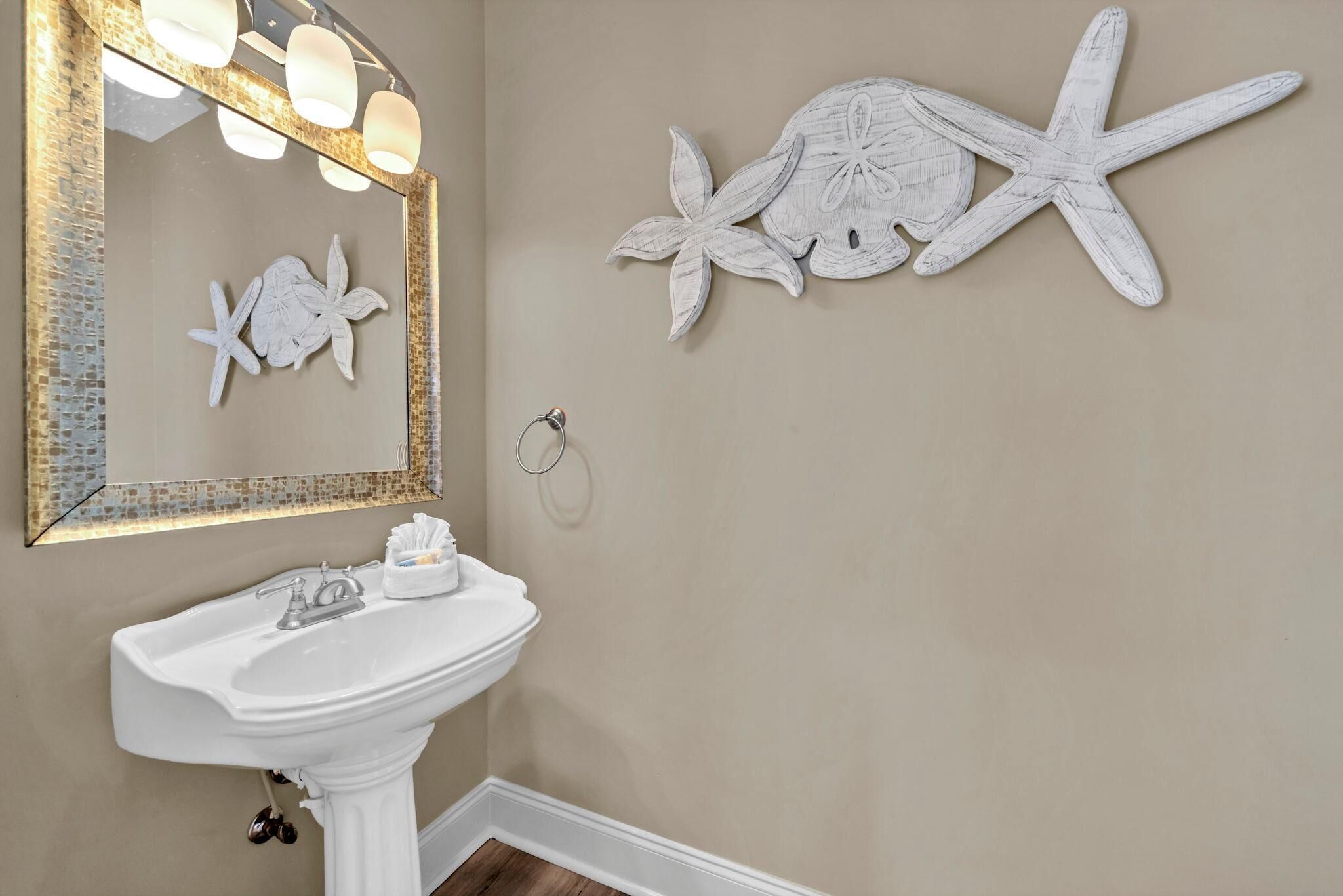 A bathroom with a white pedestal sink, a mirror with a decorative frame, and wall art of a starfish and a shell.