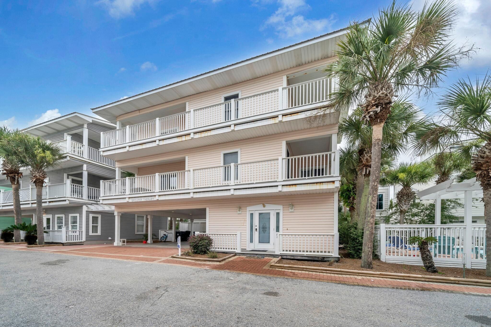 A multi-story hotel with balconies, a covered parking area, and palm trees.