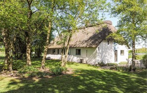 A traditional thatched-roof house surrounded by lush greenery and trees. - 2 bedroom stunning home in Bredebro (Bredebro)