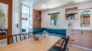 A compact living space with a dining area, kitchenette, and a blue sofa. - ZEcamping 3* piscine chauffée hammam sauna mobil-home TV LV 49m2 (Verruyes)